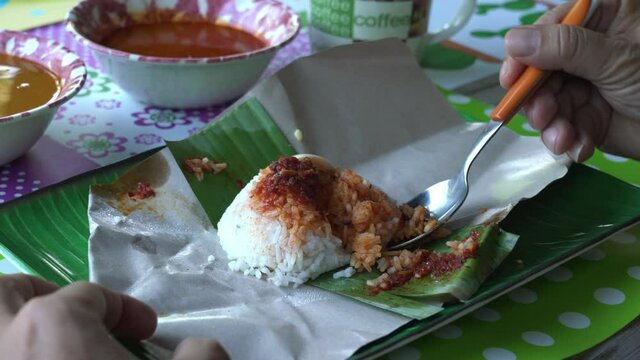 Man eating from a package of nasi lemak or Malaysia fragrant rice cooked in coconut milk added with chilly.