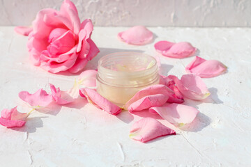 Rose oil extract pure natural face moisturizer bottle surrounded by fresh rose petals and rose flower.