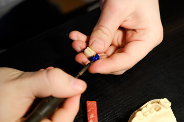 Obraz premium Dental technician modelling tooth crowns with hot wax. The hands of a dental technician close-up