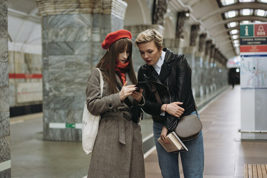young caucasian women standing on platform of metro station in Saint Petersburg, Russia. They are looking at smartphone Image with selective focus, toning and noise effect