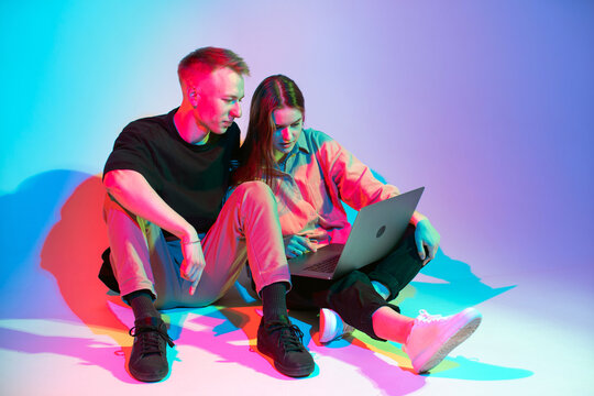 Cool team young girl and guy working on laptop creating design project. Colored neon studio light - Powered by Adobe