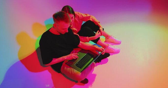 Young teen couple with laptop, working on computer oe shopping online. Colored Neon light and background