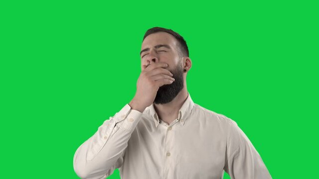 Tired overworked young business man yawning and rubbing eyes. Portrait isolated on green screen background. 