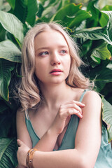 Attractive young blonde girl among a leaves of a tropical plants.Natural woman beauty.Closeness to the nature.Eco,urban jungle,biophilia concept.Summer concept.Skin care and wellness concept.