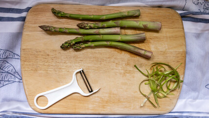Peeler and fresh green asparagus, peels of vegetable on a wooden cutting board. Top view.

