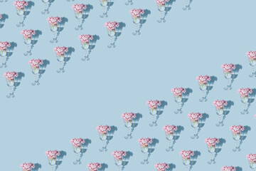 Retro minimalistic pattern concept of a glass with pink blooming flowers. Pastel blue background, geometric composition, creative spring and summer idea.