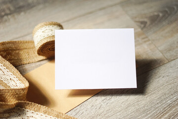 Blank white card on wooden background with a natural paper envelope and burlap ribbon. Empty space for text. Copy space.