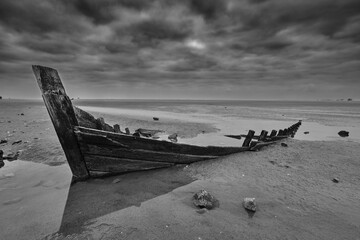 small fisherman boat semi sunk in the sand with a very dramatic cloudy sky. black and white image