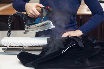 Seamstress steams a velvet jacket with an iron in her atelier. Authentic lifestyle