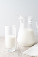 A glass and a jug of milk with a white napkin on a wooden table on white background