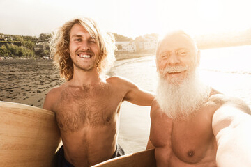 Father and son having fun doing selfie on the beach after surf session - Soft focus on left man face