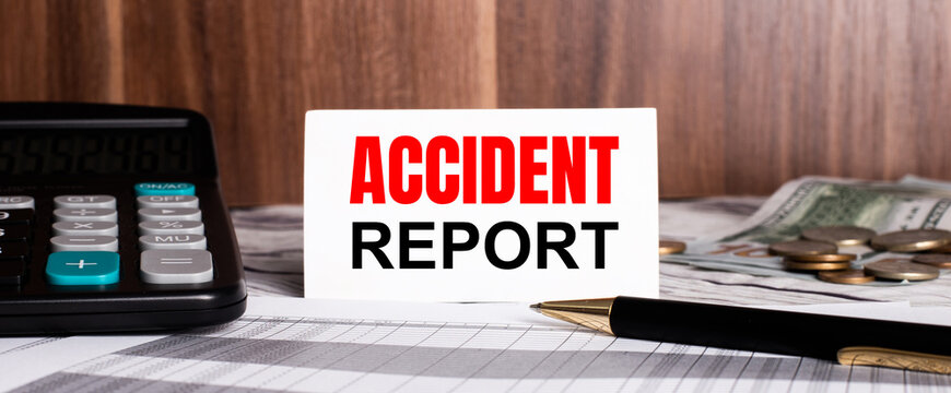 On a wooden background lies pen with calculator and white card with words ACCIDENT REPORT