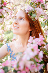Portrait of a smiling young woman with red hair and clean skin in a blooming apple orchard. Selective focus image, tinted sunlight. Close-up vertical.