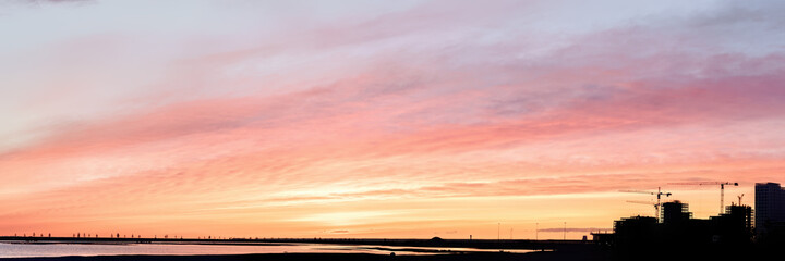 Bright sunset sky and silhouette of a construction site on it panoramic view