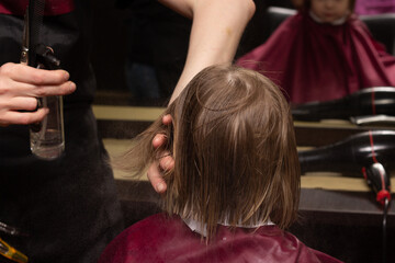 A little blonde girl 3 years old gets a bob haircut in a hairdresser. Baby hair care. Close-up.	