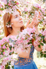 Obraz premium Young woman in blue dress reaches for pink fragrant cherry blossoms. Concept of youth and no allergy to bloom in spring.