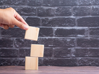 Close-up of hand holding empty wooden block on wooden table with black brick wall background. Space for text