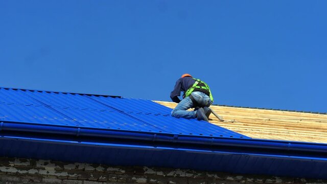 Skilled man builder in helmet removes large blue corrugated deck on roof on sunny summer day low angle shot slow motion
