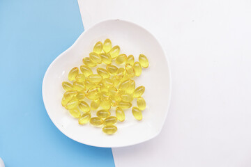 Close up of many vitamin capsule on heart shape plate on color background 