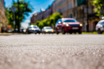 Summer in the city, the cars drive down the street with trees. Close up view from the asphalt level