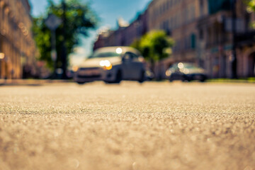 Summer in the city, the headlights of an approaching car on the street with trees. Close up view from the asphalt level