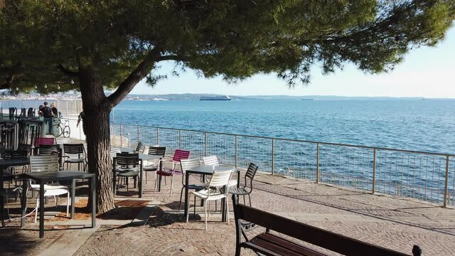 Tables, chairs and a bench along Barcola seafront in Trieste, Italy,  during a glorious springtime afternoon, with the city skyline in the background