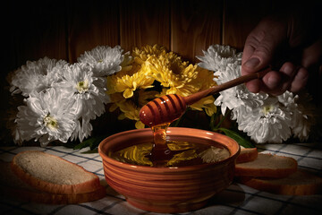 Honey is pouring from a spoon into a cup on the table with fresh bread on a background of flowers.