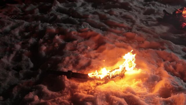 Burning sword lies on the snow after the battle is over. Winter night low light.