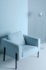 A light blue lamp and soft armchair against a plain wall. Minimalism in interior design