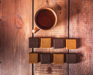 Delicious dessert with sweets of iris of two colors and a mug with tea on a wooden brown tray