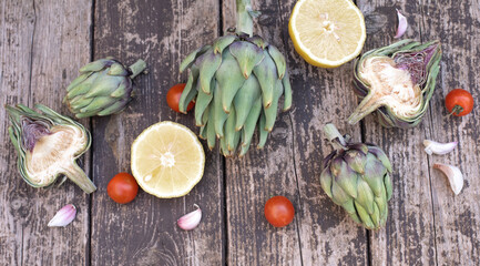 Big artichoke decorate by cutting half lemon and artichoke with garlic and tomato cherry. Vegetables on wooden background. Concept very healthy full of vitamins food for diet. Close-up.