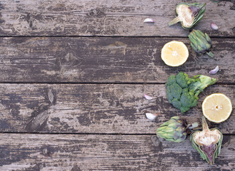 Artichoke, broccoli and halves lemon on wooden background decorate with garlic. Concept very healthy and green full of vitamins vegetables food. Top view, copy space for text. Large banner