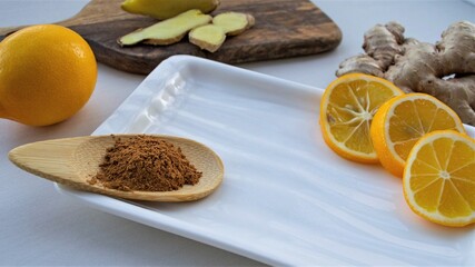 Wooden spoon with cinnamon and health ingredients on a white glazed plate (ginger, lemon)