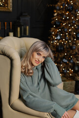 Beautiful and emotional woman on an armchair by a Christmas tree.