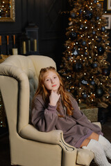 Beautiful teenage girl on an armchair by the Christmas tree.