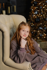 Beautiful teenage girl on an armchair by the Christmas tree.