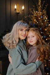 Beautiful and happy mother with her daughter at the New Year tree.
