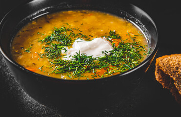 Soup with pickled cucumbers and pearl barley in black bowl on black wooden table background