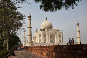 Side view of the Taj Mahal. View through the trees. People walking by. Here in the shade one finds protection from the oppressive heat. Normal perspective. Day.