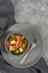 Healthy vegetable salad of tomatoes and cucumbers in a gray plate with a gray napkin on a gray concrete background. Diet menu concept. View from above. copy place
