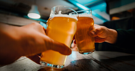 Closeup view of a two glass of beer in hand. Beer glasses clinking in bar or pub