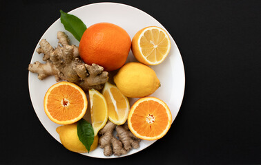 citruses on a white plate, oranges, lemons and ginger on a white plate on a black background.