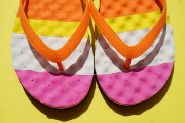 Closeup colored beach flip flops on a sunny yellow table.