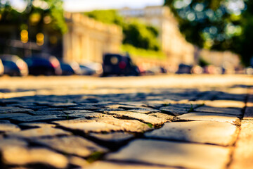 Summer in the city, the sunlit empty old street paved with stone near the park and parked cars....