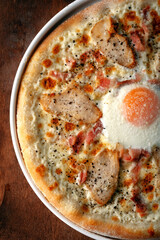 Half Homemade Carbonara pizza with bacon and chicken breast, egg and cheese on a wooden background. Unconventional pizza recipes