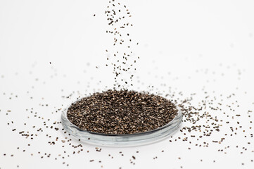 chia seeds on a white background in a glass bowl, the seeds are poured from above, frontal view,...