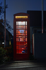 Fototapeta premium Boy reading at night in a red telephone box filled with books