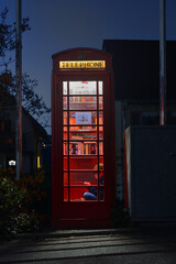 Boy reading at night in a red telephone box filled with books
