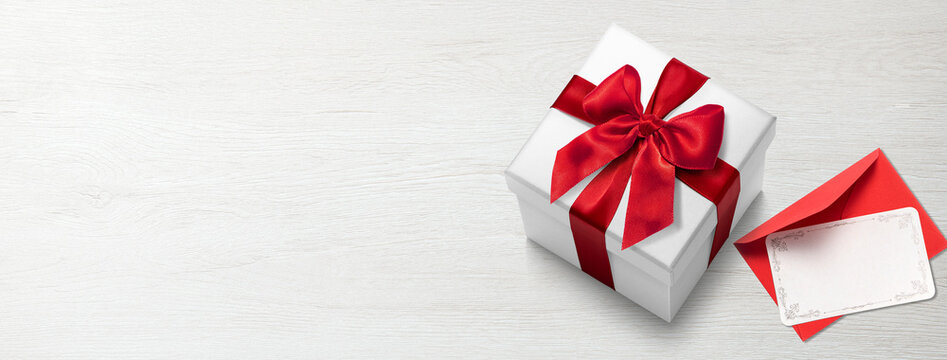 白木のテーブルの上に置かれた赤いリボンをかけたプレゼントの箱。空白のメッセージカード。