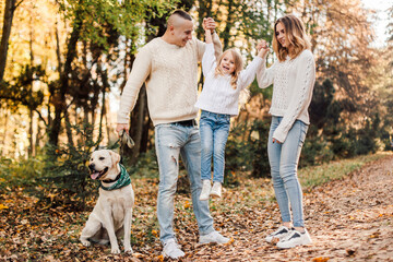 Obraz premium Happy beautiful family with dog labrador is having fun together walking the in park.